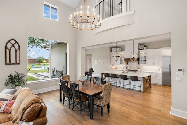 dining space with plenty of natural light, light wood finished floors, a towering ceiling, and an inviting chandelier