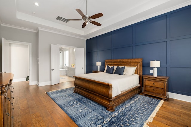 bedroom featuring a tray ceiling, visible vents, hardwood / wood-style flooring, and a decorative wall