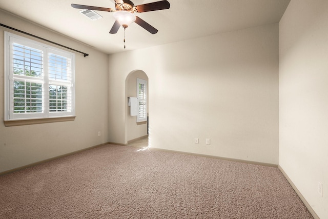 carpeted empty room with a ceiling fan, arched walkways, visible vents, and baseboards
