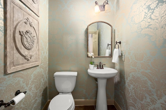 half bathroom featuring a sink, baseboards, wallpapered walls, and toilet