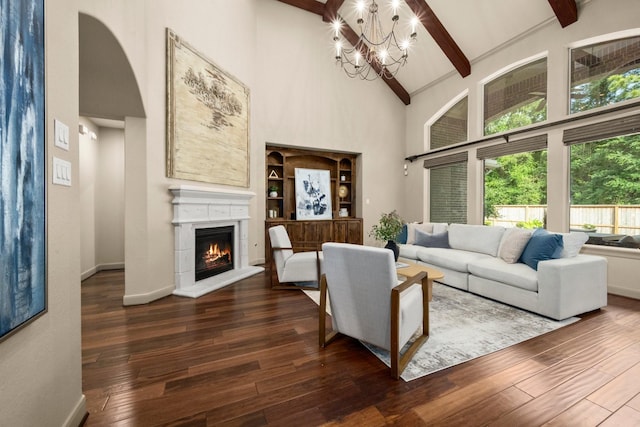 living room with an inviting chandelier, beam ceiling, high vaulted ceiling, a lit fireplace, and hardwood / wood-style flooring