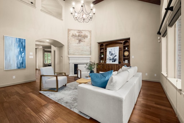 living area with arched walkways, a high ceiling, a chandelier, and wood finished floors