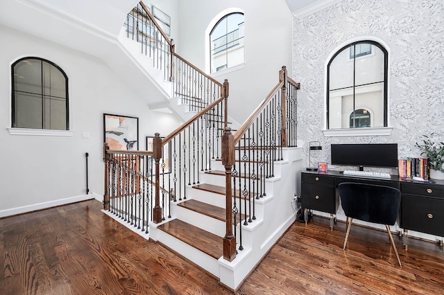 stairway featuring baseboards, wood finished floors, and a towering ceiling