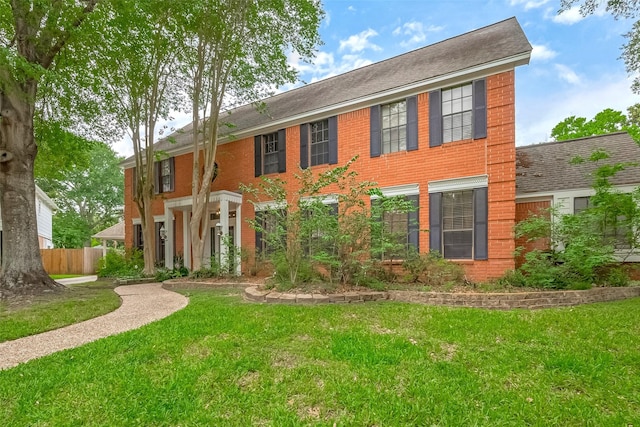 colonial house featuring fence, a front lawn, and brick siding
