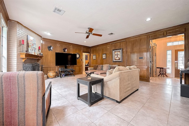 living room with wooden walls, crown molding, a ceiling fan, and visible vents