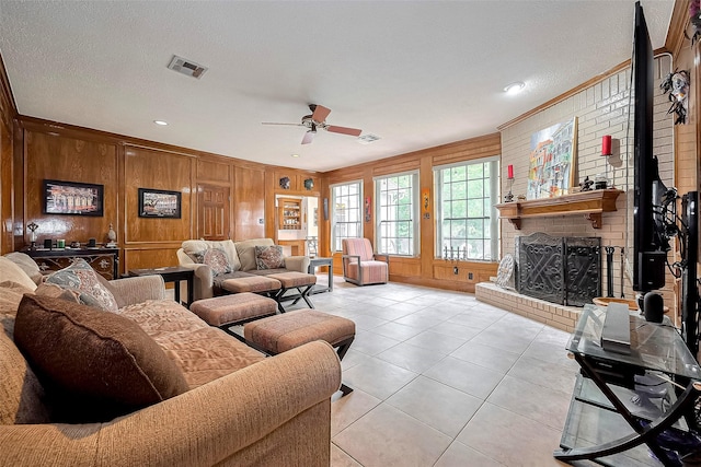 living room with a ceiling fan, wood walls, light tile patterned flooring, and visible vents