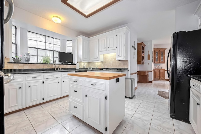 kitchen featuring white cabinets, a sink, freestanding refrigerator, tasteful backsplash, and butcher block counters
