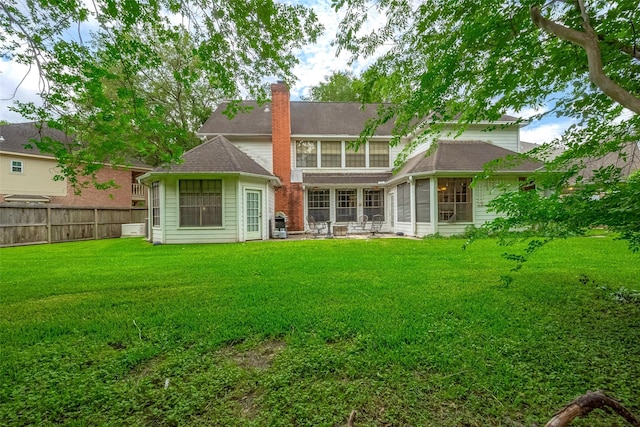 back of property with a chimney, roof with shingles, a lawn, a sunroom, and fence