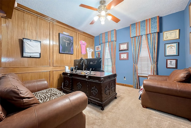 carpeted office space with baseboards, wood walls, a textured ceiling, and ceiling fan