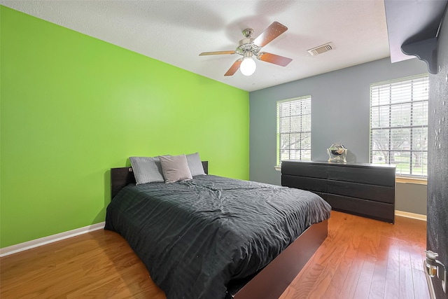 bedroom featuring baseboards, a ceiling fan, wood finished floors, and visible vents