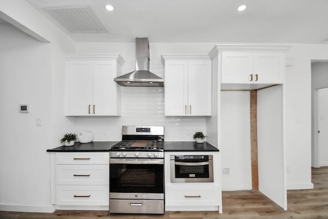 kitchen featuring visible vents, dark countertops, wall chimney range hood, white cabinetry, and appliances with stainless steel finishes
