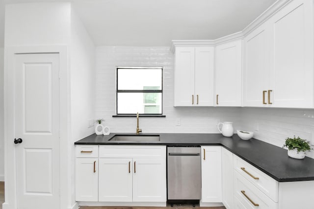 kitchen featuring dark countertops, tasteful backsplash, stainless steel dishwasher, a sink, and white cabinetry
