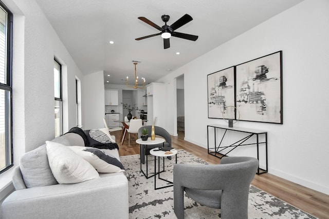 living room with recessed lighting, plenty of natural light, ceiling fan with notable chandelier, and light wood-type flooring