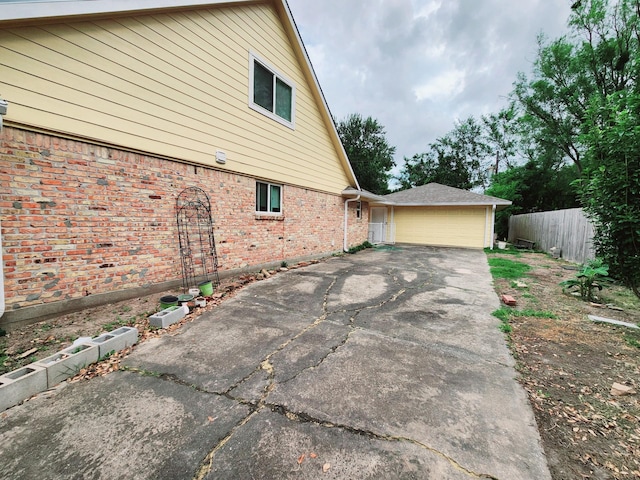 view of property exterior with fence, a garage, a patio area, and brick siding