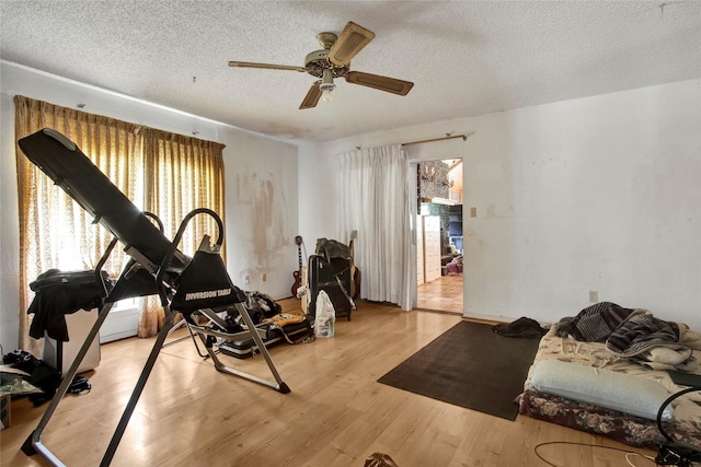 exercise room featuring a textured ceiling, ceiling fan, and light wood finished floors