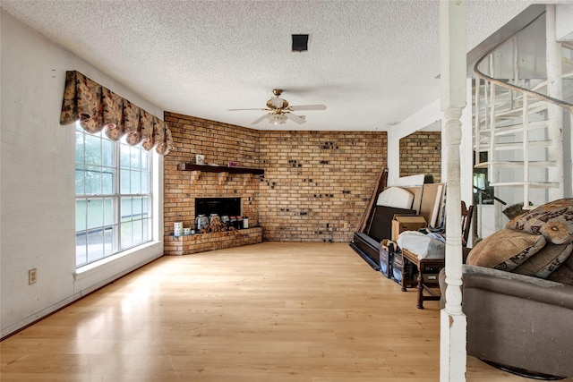living room featuring a textured ceiling, ceiling fan, brick wall, and wood finished floors