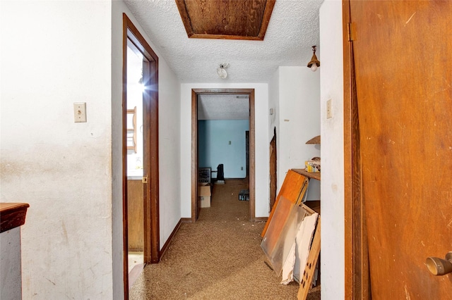 hallway featuring carpet floors, a textured ceiling, and baseboards
