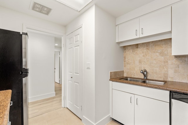 kitchen featuring visible vents, stainless steel dishwasher, a sink, white cabinets, and freestanding refrigerator