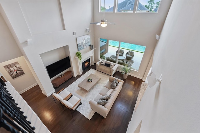 living room featuring plenty of natural light, a lit fireplace, wood finished floors, and a towering ceiling