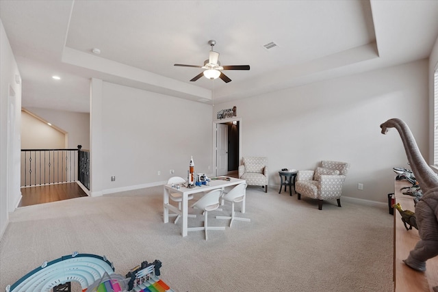 living area featuring ceiling fan, visible vents, a raised ceiling, baseboards, and carpet