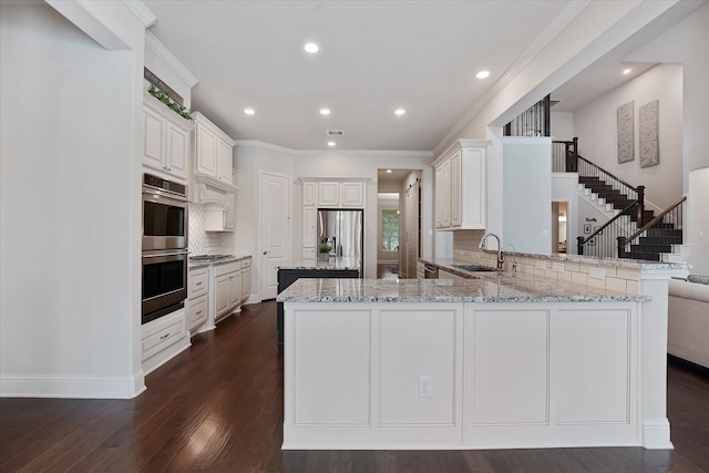 kitchen with decorative backsplash, a peninsula, light stone counters, a sink, and appliances with stainless steel finishes