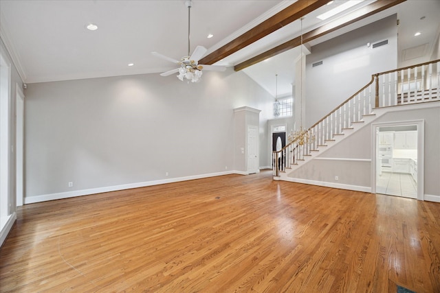 unfurnished living room with ceiling fan, beam ceiling, wood finished floors, stairway, and baseboards