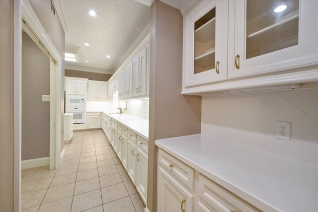 kitchen with crown molding, light tile patterned flooring, white appliances, light countertops, and backsplash