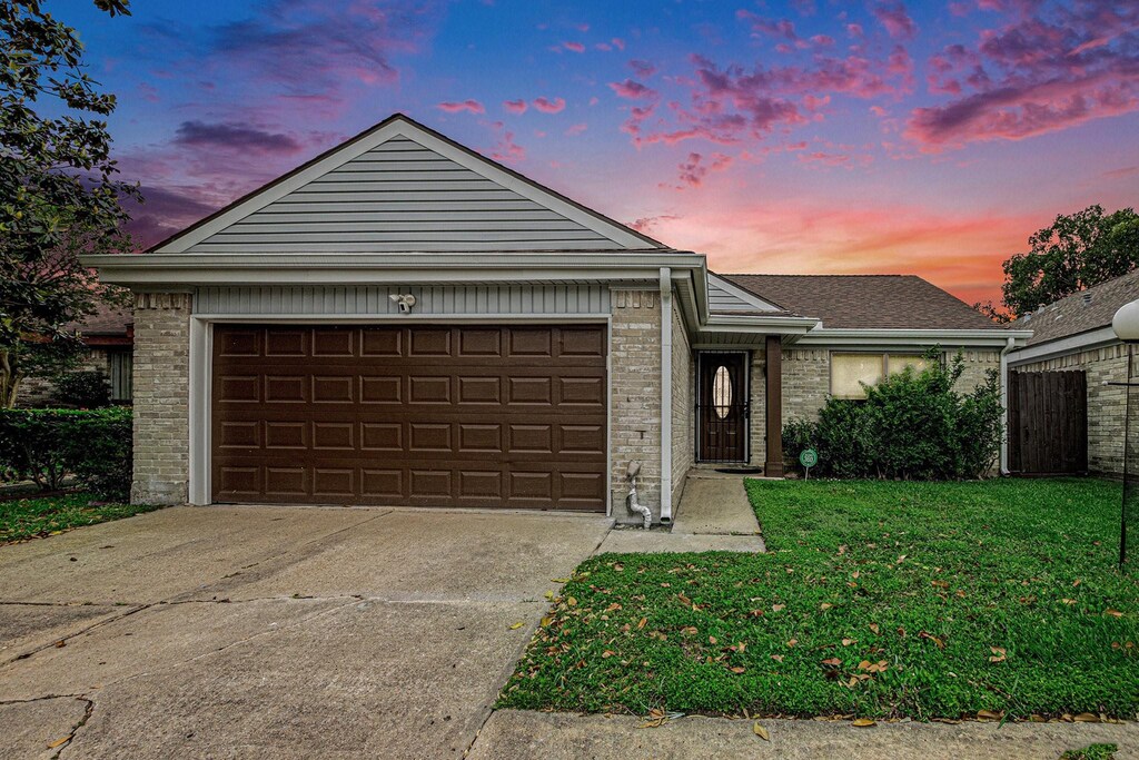 ranch-style home featuring a garage, a lawn, driveway, and brick siding