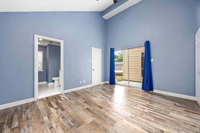 unfurnished bedroom featuring baseboards, high vaulted ceiling, wood finished floors, and ensuite bath