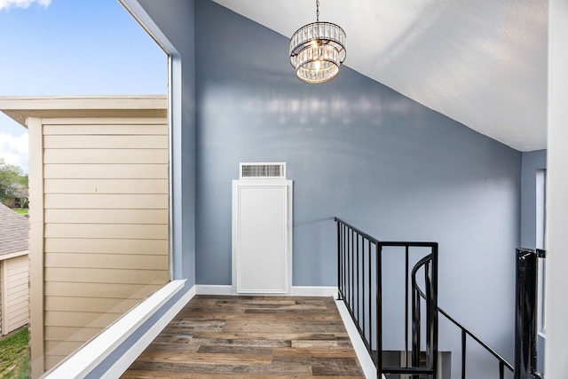 staircase featuring visible vents, a notable chandelier, wood finished floors, baseboards, and lofted ceiling