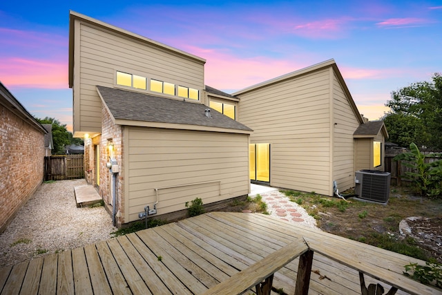 back of property at dusk with central AC unit, fence, a deck, and a shingled roof