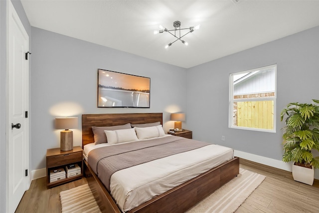 bedroom with an inviting chandelier, baseboards, and wood finished floors