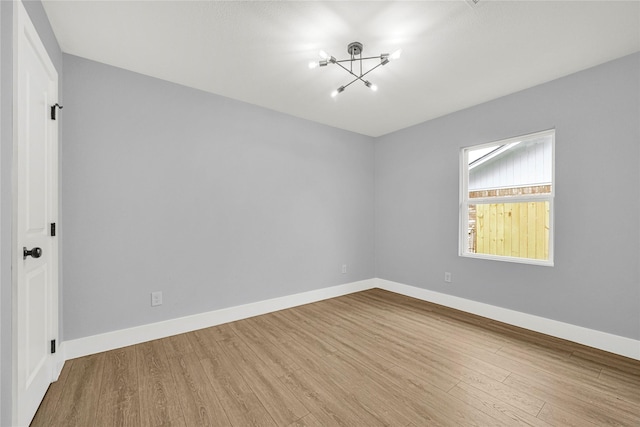 empty room featuring baseboards, wood finished floors, and a notable chandelier