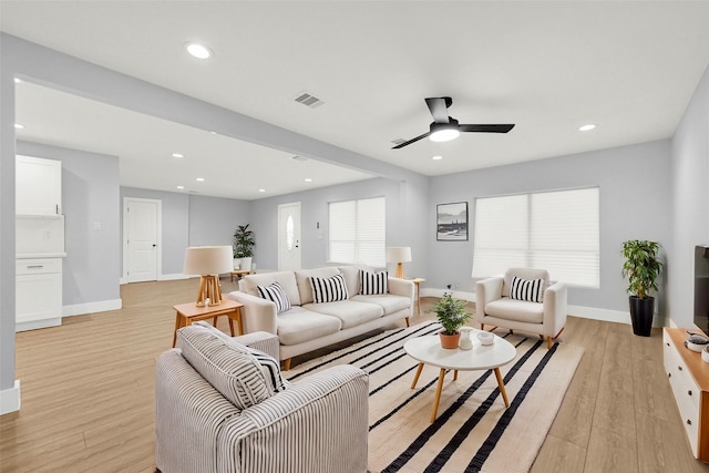 living room featuring a ceiling fan, baseboards, visible vents, and light wood finished floors