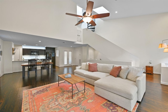 living room featuring dark wood-type flooring, baseboards, ceiling fan, and high vaulted ceiling
