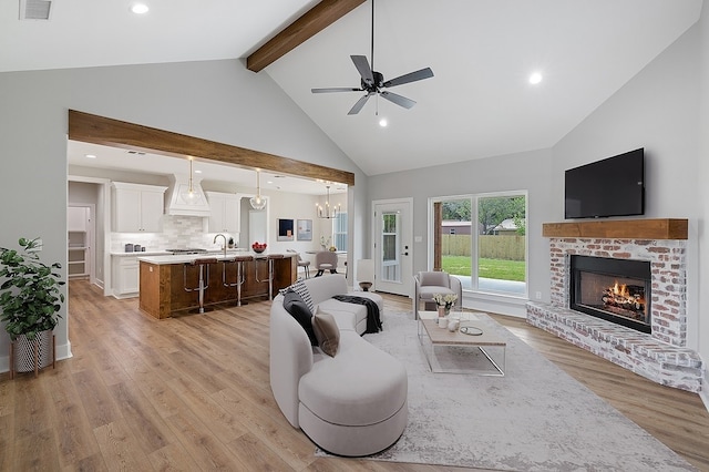 102 Tekla St, Weimar, TX 78962 - living room featuring a brick fireplace, beam ceiling, high vaulted ceiling, light wood finished floors, and ceiling fan with notable chandelier