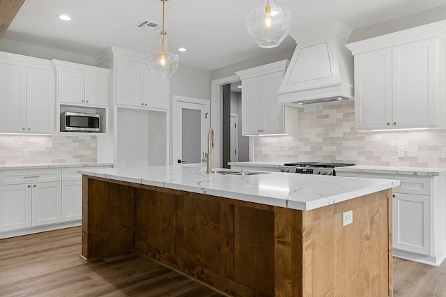 102 Tekla St, Weimar, TX 78962 - kitchen featuring visible vents, custom exhaust hood, a center island with sink, stainless steel microwave, and a sink