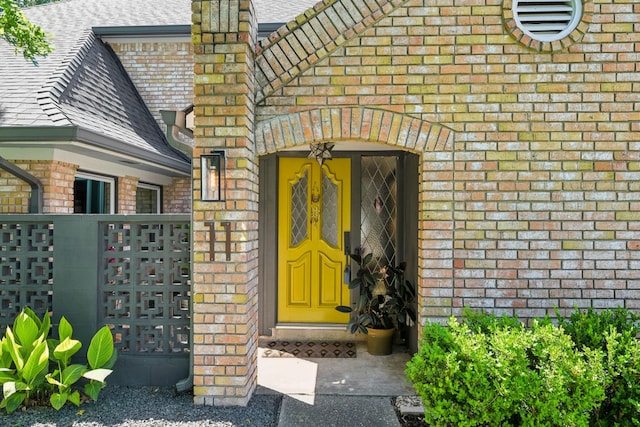 view of exterior entry featuring brick siding and a shingled roof