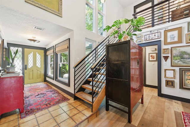 entrance foyer featuring baseboards, a wealth of natural light, a towering ceiling, and visible vents