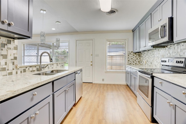 kitchen featuring gray cabinets, decorative backsplash, appliances with stainless steel finishes, a sink, and light wood finished floors