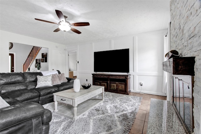 21426 Park York Dr, Katy, TX 77450 - tiled living area with a ceiling fan, a stone fireplace, a textured ceiling, a decorative wall, and stairs