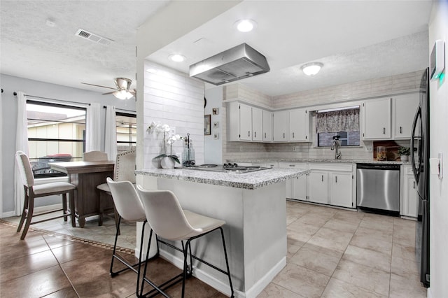 21426 Park York Dr, Katy, TX 77450 - kitchen with wall chimney range hood, stovetop, a textured ceiling, dishwasher, and a peninsula