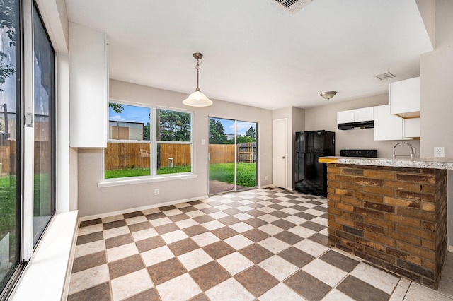 kitchen with freestanding refrigerator, white cabinetry, baseboards, under cabinet range hood, and visible vents