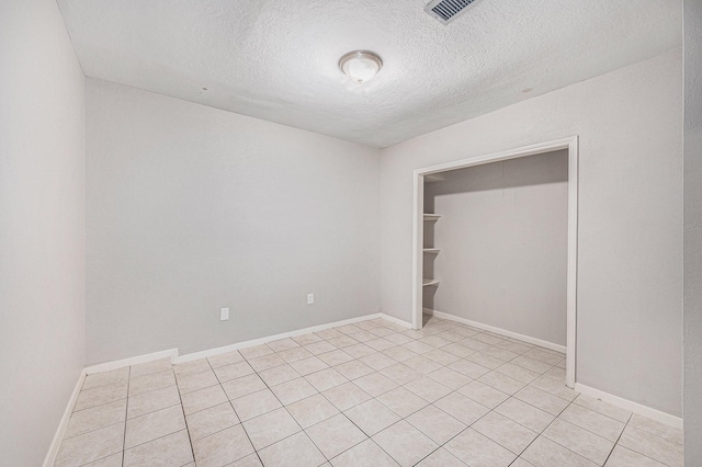 unfurnished bedroom featuring visible vents, baseboards, a textured ceiling, and light tile patterned floors