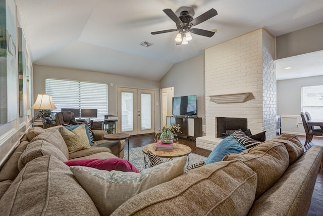 living area with french doors, a ceiling fan, visible vents, a brick fireplace, and wood finished floors