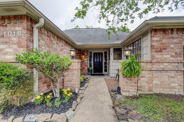 entrance to property with roof with shingles and brick siding