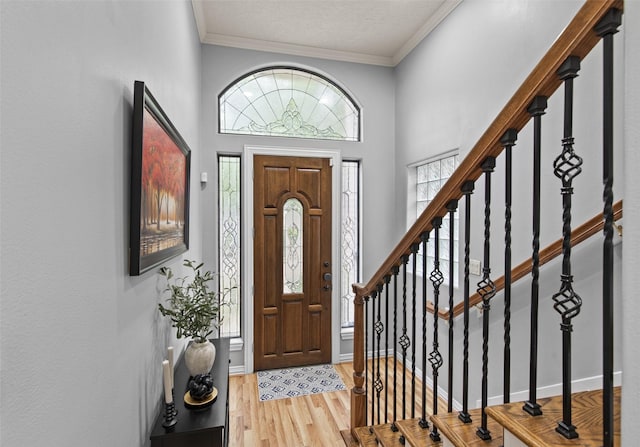 foyer with stairs, a textured ceiling, ornamental molding, and wood finished floors