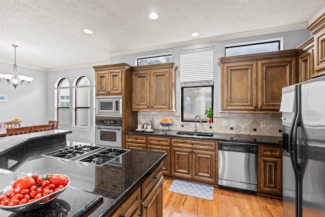 kitchen featuring a textured ceiling, appliances with stainless steel finishes, a sink, a notable chandelier, and ornamental molding