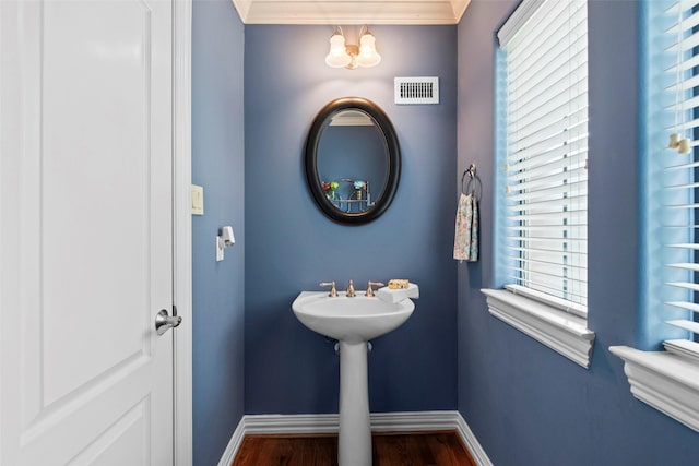 bathroom with crown molding, plenty of natural light, baseboards, wood finished floors, and visible vents
