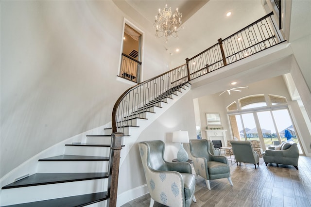 23935 Birchwood Lake Ln, Katy, TX 77493 - staircase with a fireplace, ceiling fan with notable chandelier, baseboards, wood finished floors, and a towering ceiling